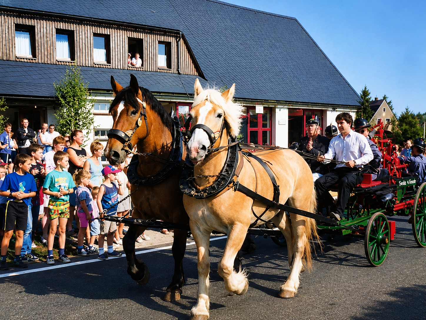 Karino und Portos ziehen eine historische Feuerwehrspritze durch Grumbach; Zuschauer säumen beim Dorffest 1998 die Straße.
